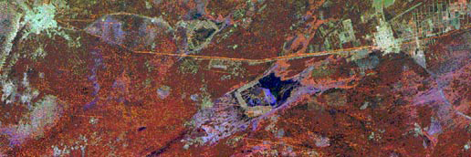 This image was taken by a low-orbit satellite using radar to show the location of the Great Wall if it was to be seen from space. There are areas of dark red, some of a lighter mint green color, and then areas of purple. In the upper center of the photo, there is an orange very very thin curve that shows the location of the Great Wall of China, where it vaguely appears from space on radar.