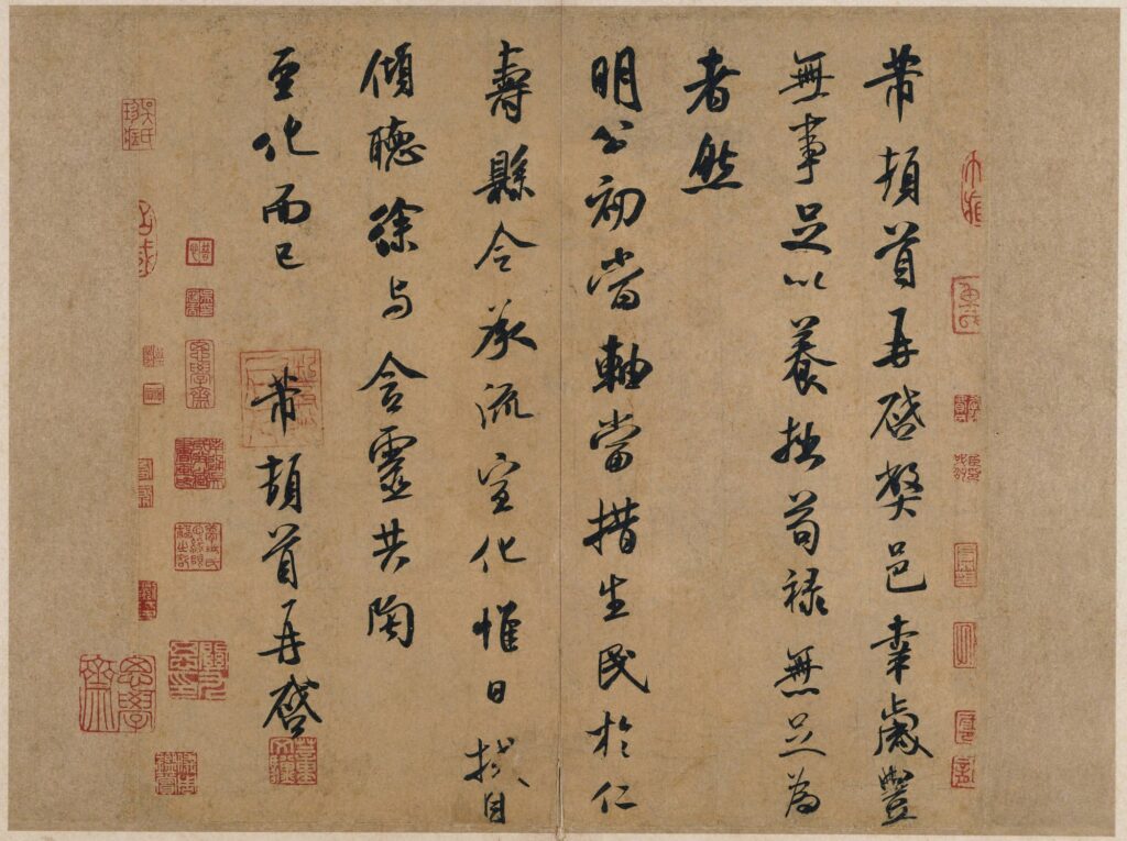 The image shows an example of Chinese calligraphy. The writing is written top to bottom with different characters, including spaces at some parts. The writing is all evenly spaced out. There are also red seals placed throughout the work around the frame of the calligraphy with one red seal on top of the calligraphy on the left side of the paper.