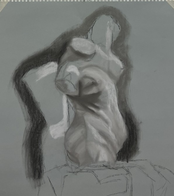 The image is on a large gray scale paper. Charcoal was used to draw a bust of a woman's body, the left arm is raised towards the ceiling while the other arm is staying at the side. There is a curve and twists in the body, defined using shading. There are also dark outlines defining the body.